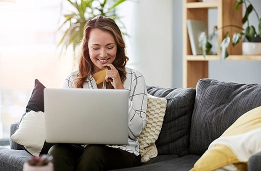 Happy BCN Services client on couch with laptop